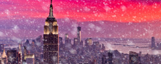 Snow falling in New York City with a vibrant pink and purple sunset in the background.