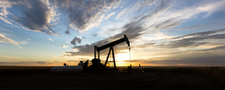Silhouette of an oil well operating against a skyline at dawn.