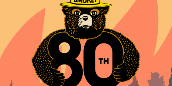 Image of Smokey Bear holding "80th Birthday" letters with fire burning in the background.