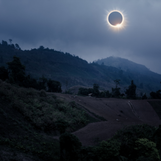 Total solar eclipse over a foggy mountain landscape.