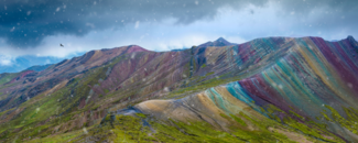 Vinicunca Rainbow Mountain in Peru with a black bird flying overhead and rain drops collecting on the lens of the camera taking the photo.