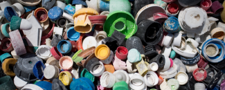 Multiple different colored caps and bottles gathered into a sizable pile with sand visible on the macroplastic debris.